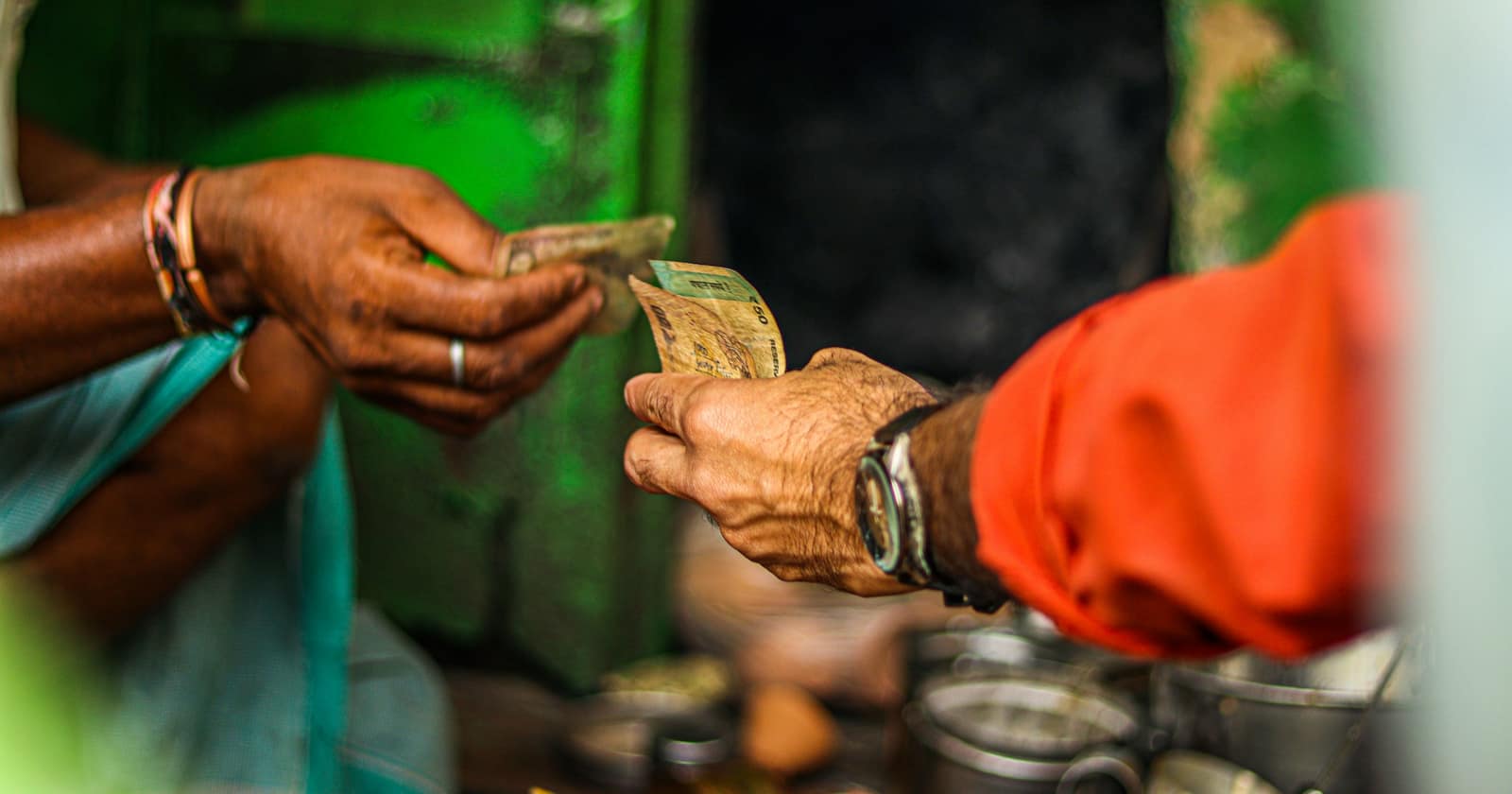 One hand passing a banknote to another across the counter of a small shop